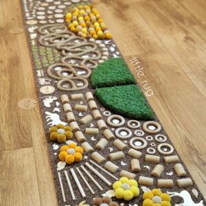 Little rug - Senzomotorický koberec na pieskovom koberci so žltým gumeným balančným ježkom, korkovými zátkami, krúteným jutovým lanom, drevenými krúžkami a plátkami, farebnou dúhou z bambuliek, kvetmi z bambuliek, umelou trávou a nočnými žiariacimi kamienkami.